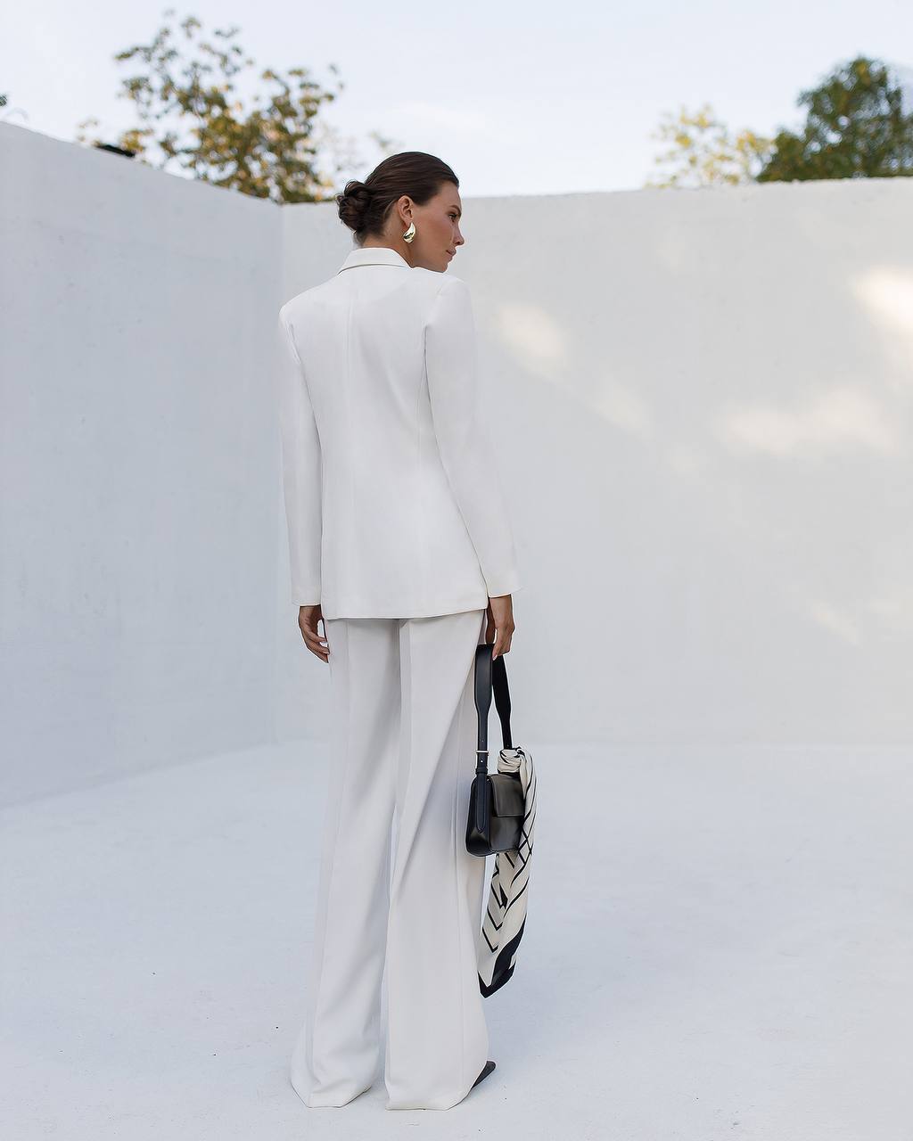 Person wearing a white outfit with a black and white bag against a light background