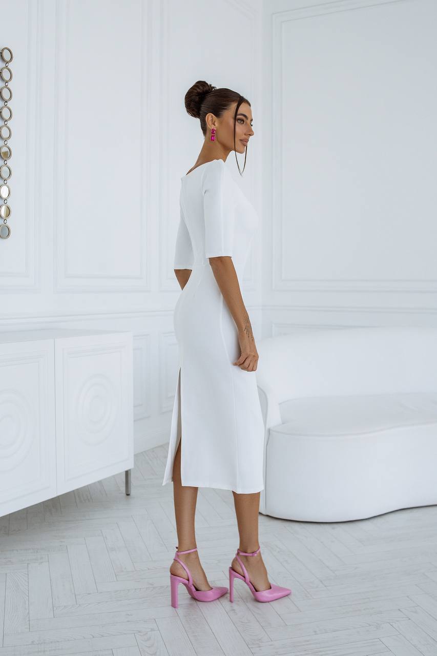 Woman in a white dress with pink high heels standing in a minimalistic room.