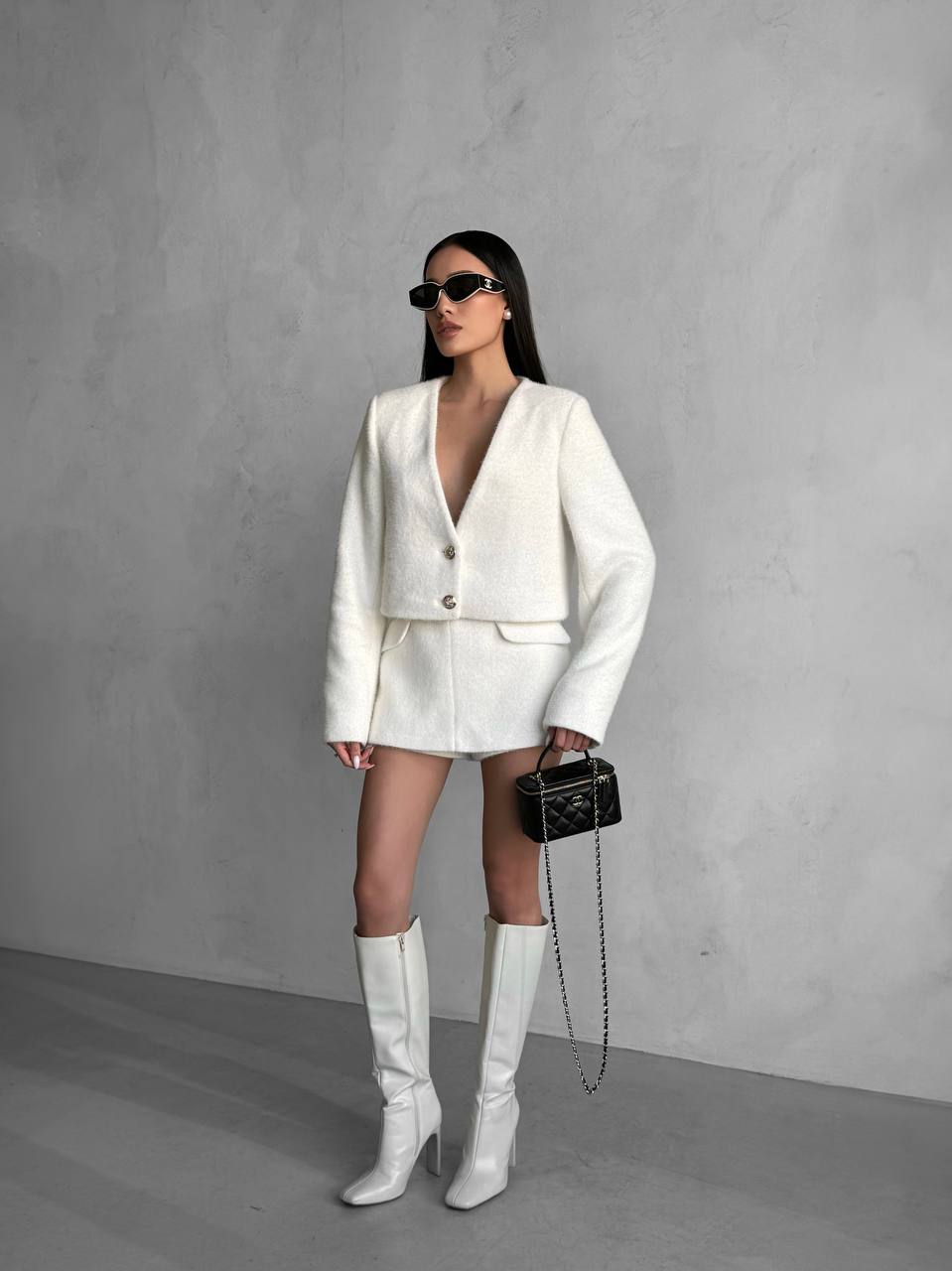 Woman in a white outfit with knee-high boots against a gray background