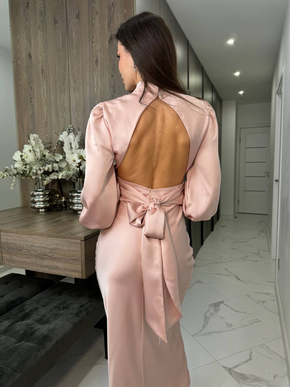 Woman in a pink satin dress standing in a modern interior setting.