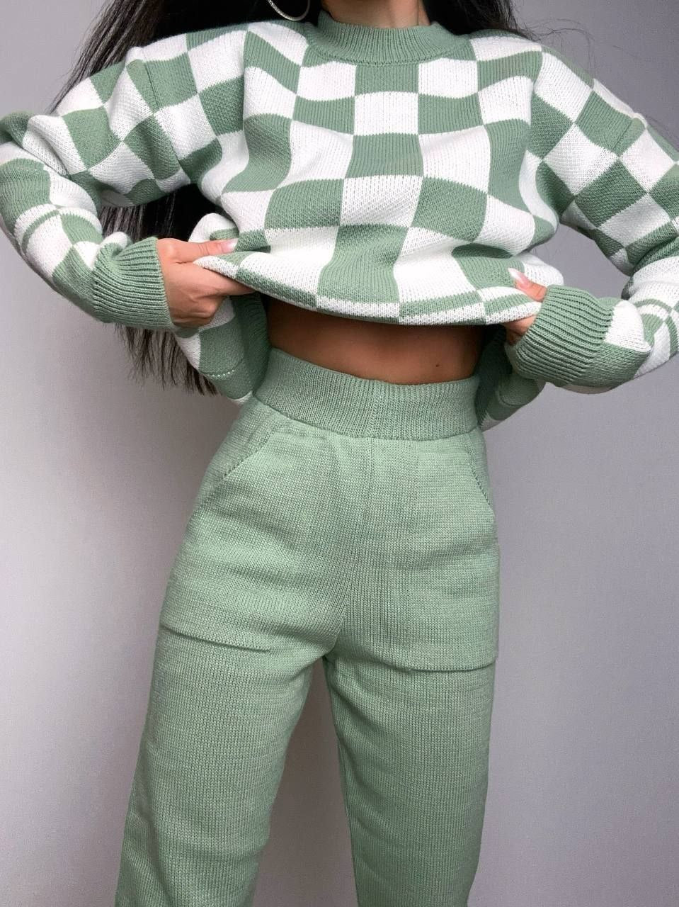 Person wearing a green and white checkered sweater and matching pants against a gray background