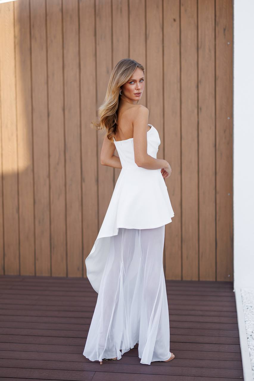 Woman wearing a white strapless dress with sheer overlay against a wooden wall.