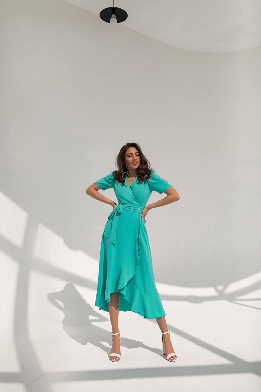 Woman in a teal dress posing against a white wall with shadows.