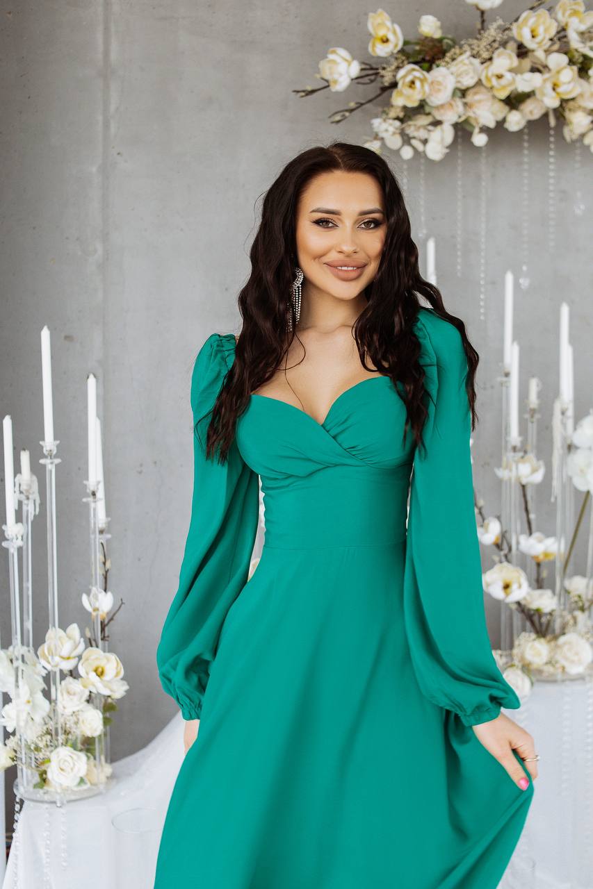 Woman in a teal dress standing in a decorated room with flowers and candles.