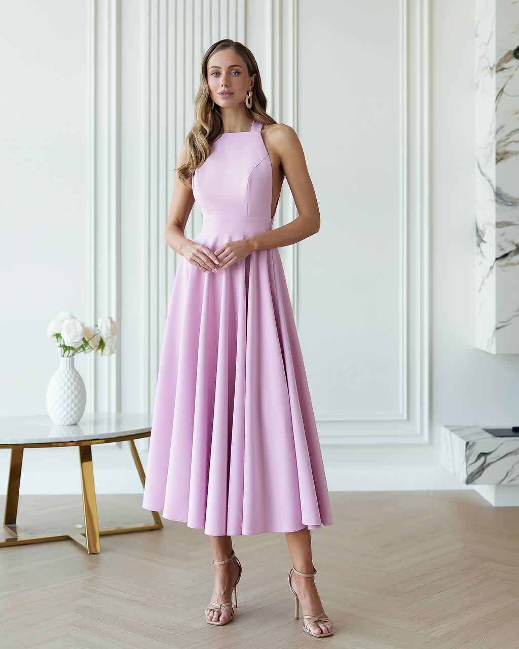 Woman wearing a pink dress standing in a stylish room with decor elements.