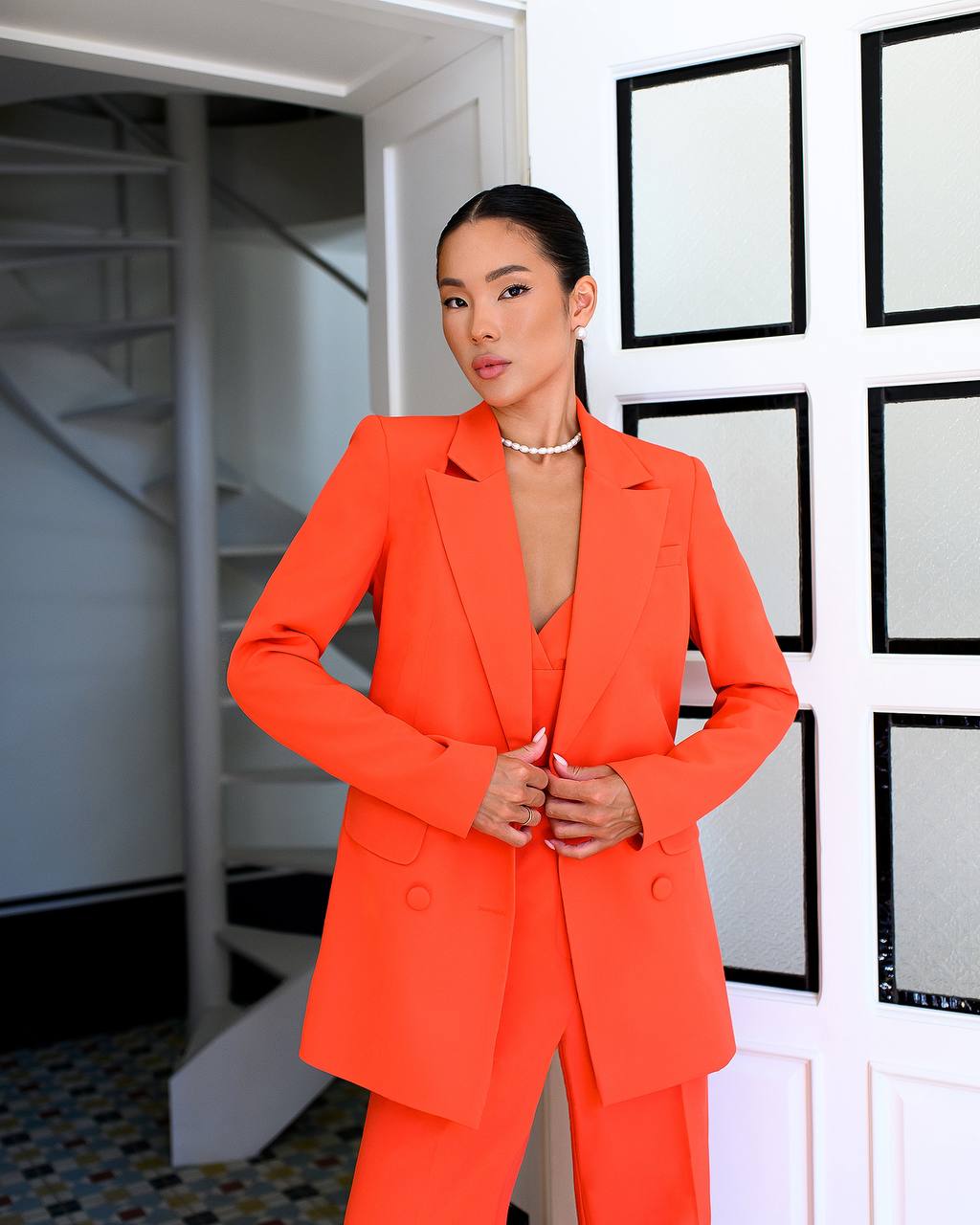 Woman wearing a bright orange suit standing in a room with white walls and framed pictures.