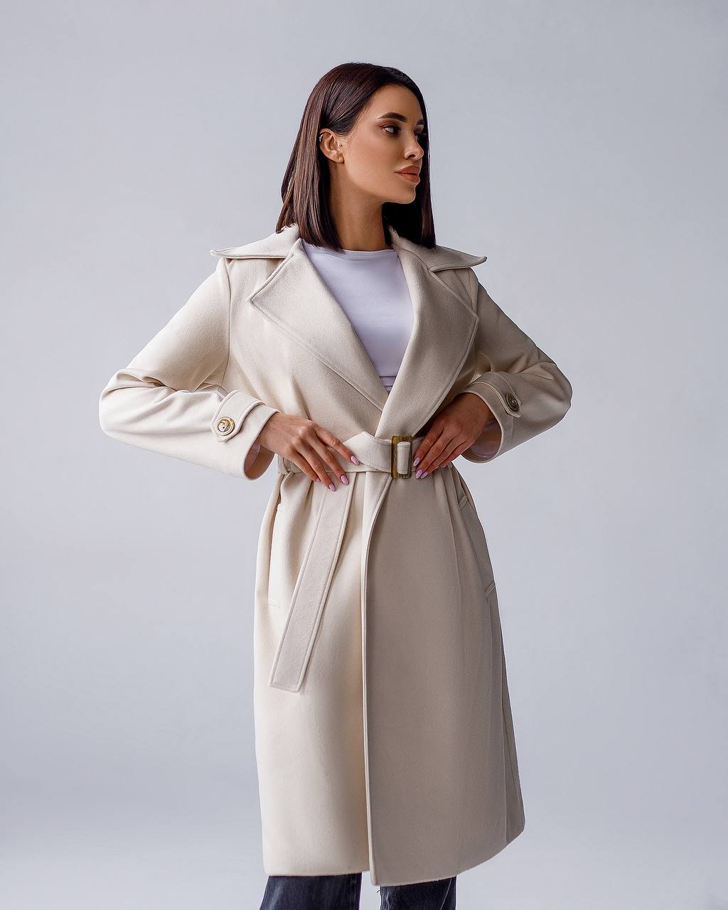 Woman wearing a beige trench coat against a plain background