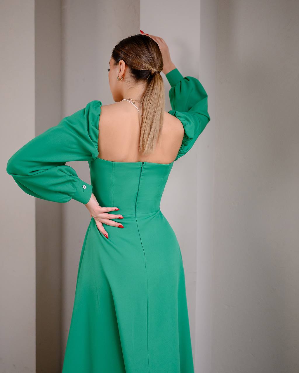 Woman wearing a green dress with long sleeves and a plain background