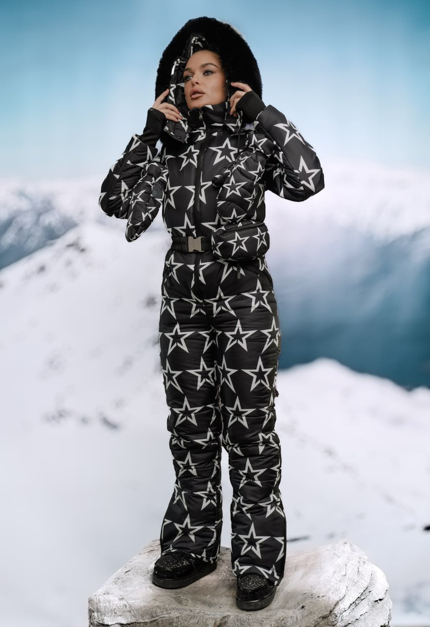 Person wearing a black snowsuit with white star patterns against a snowy mountain background