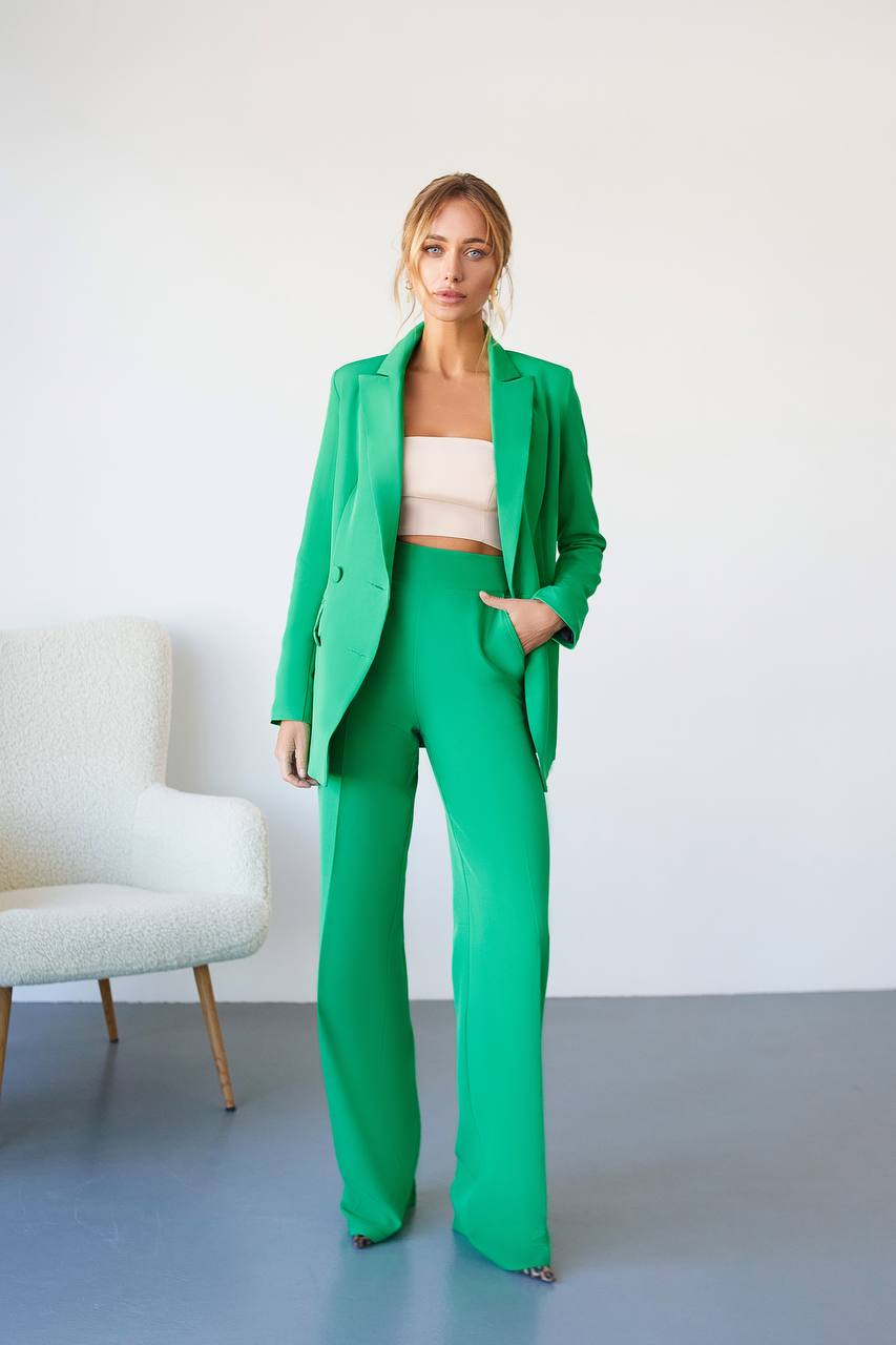 Woman in a green suit standing in a minimalistic room with a white chair.
