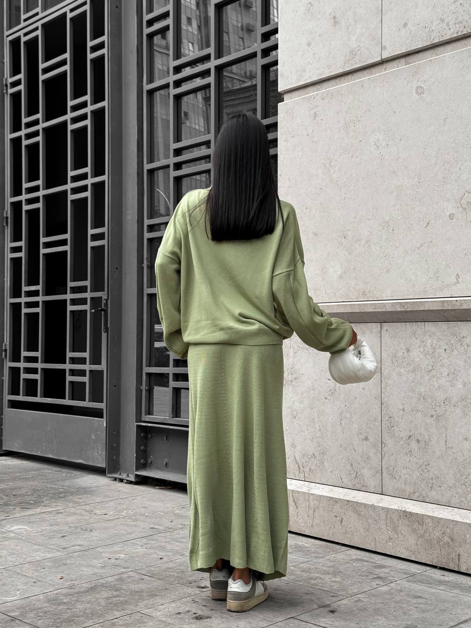 Person wearing a green outfit standing in front of a modern building entrance.