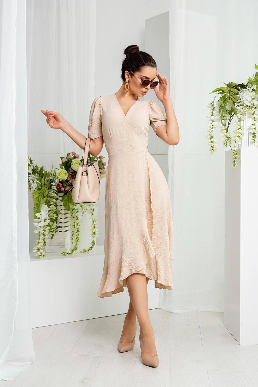 Woman in a beige dress standing in a bright room with plants.