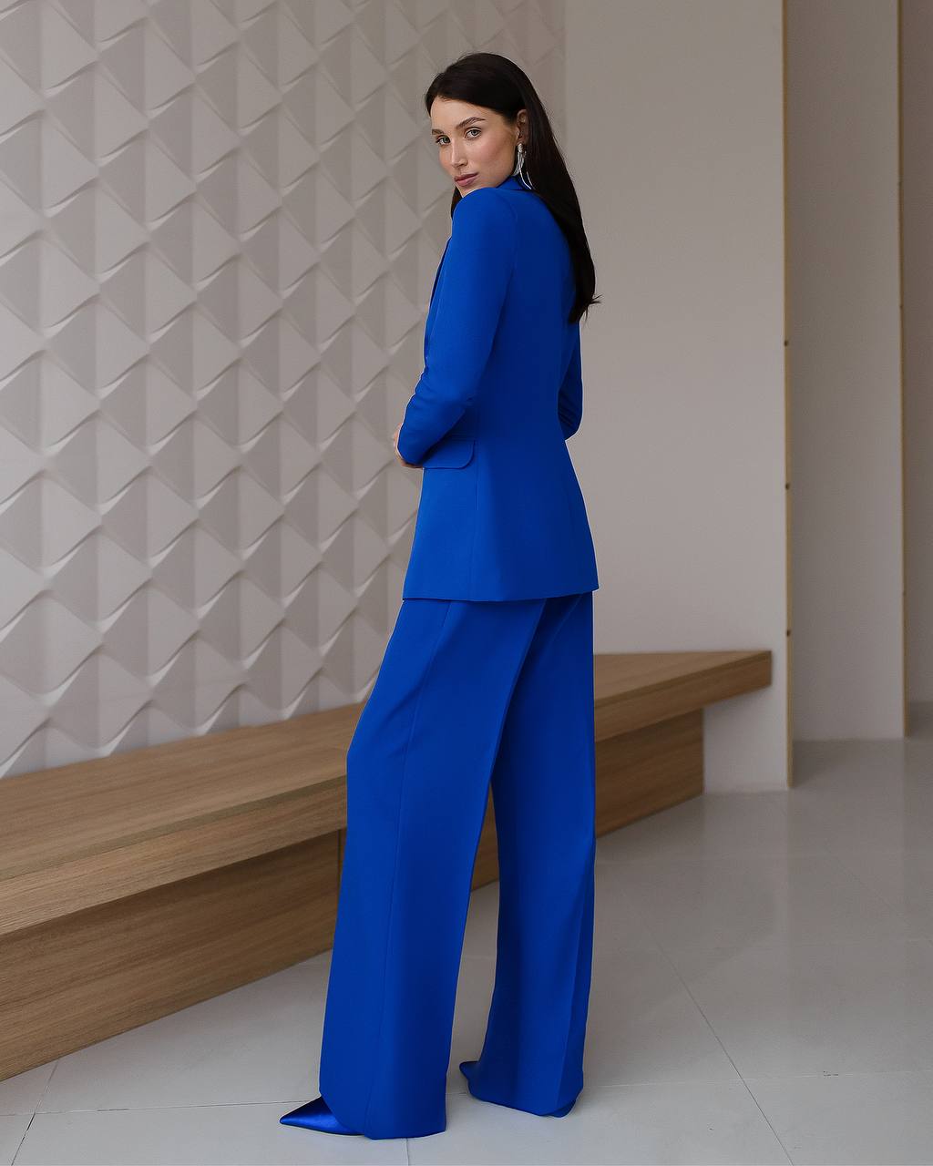 Woman wearing a blue suit standing against a textured wall.