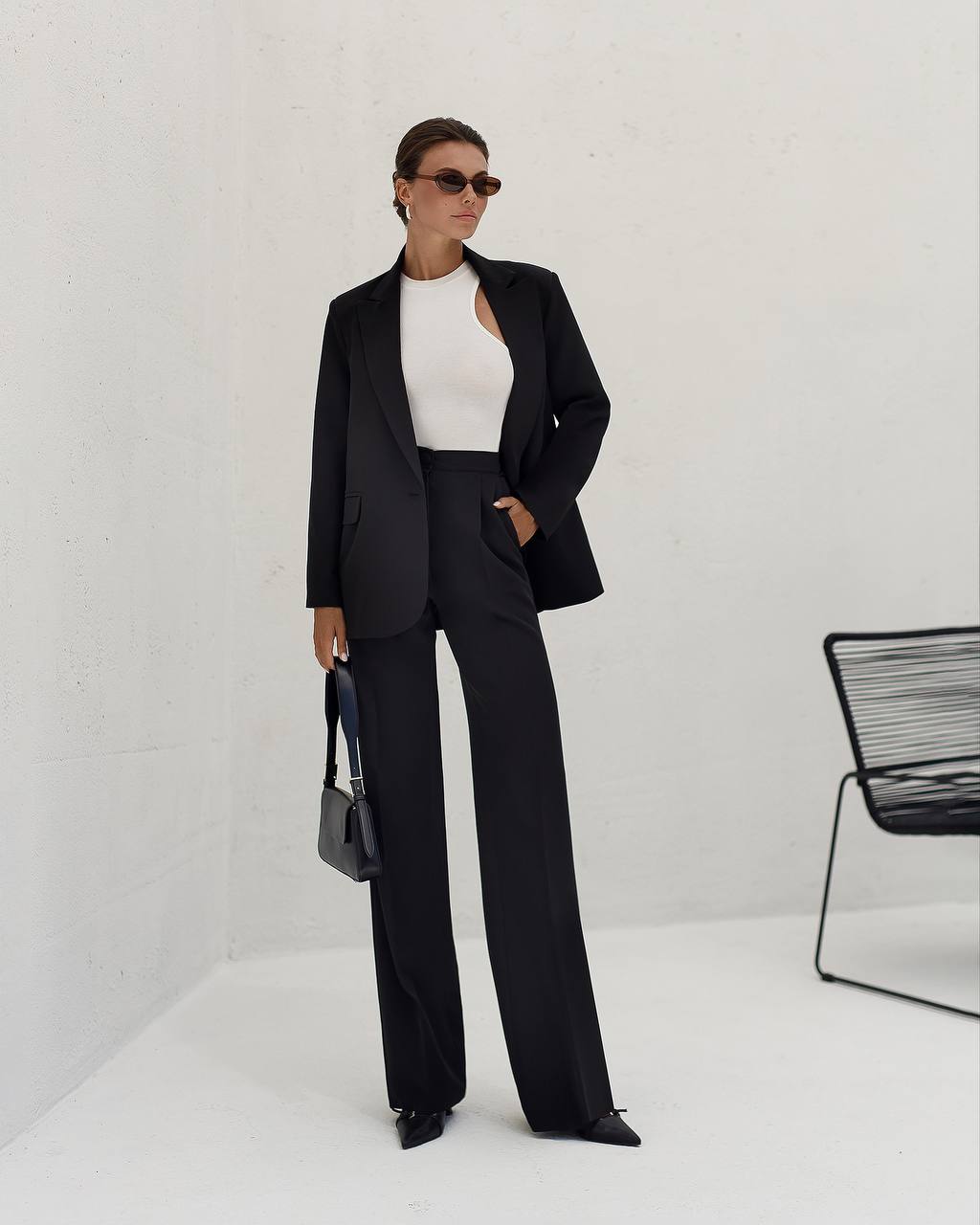 Person wearing a black suit with a white top, standing against a plain background.
