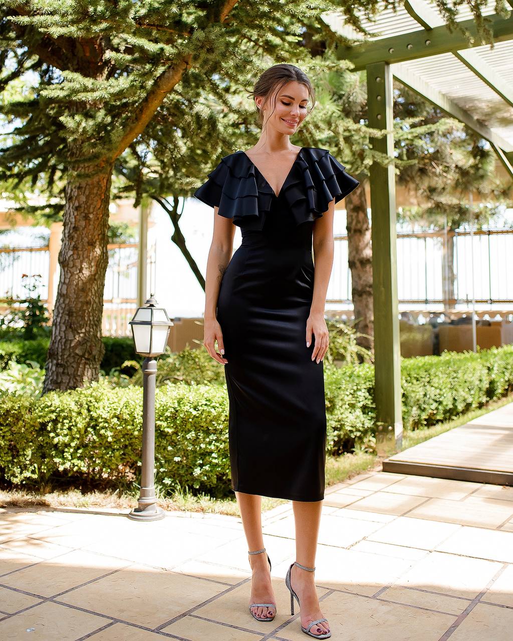Woman in a black dress standing outdoors with trees and a building in the background