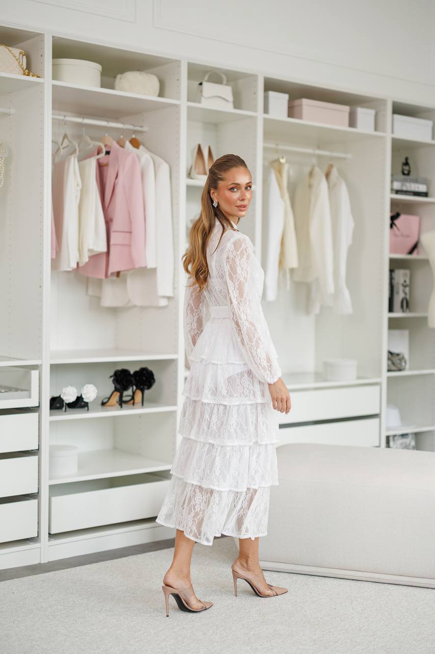 Woman in a white lace dress standing in a modern closet with shelves and clothing.