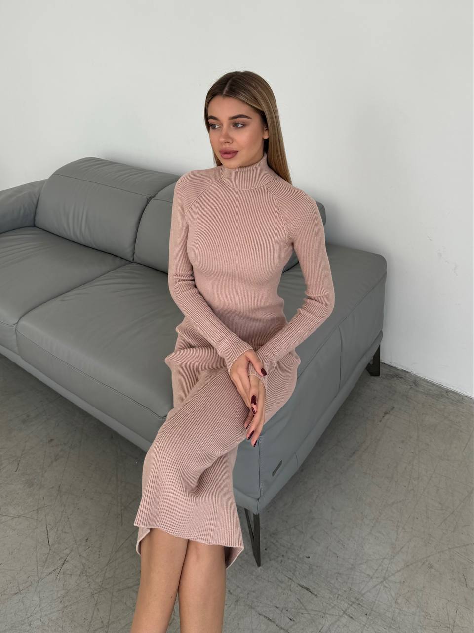 Woman in a pink dress sitting on a gray sofa against a white wall.