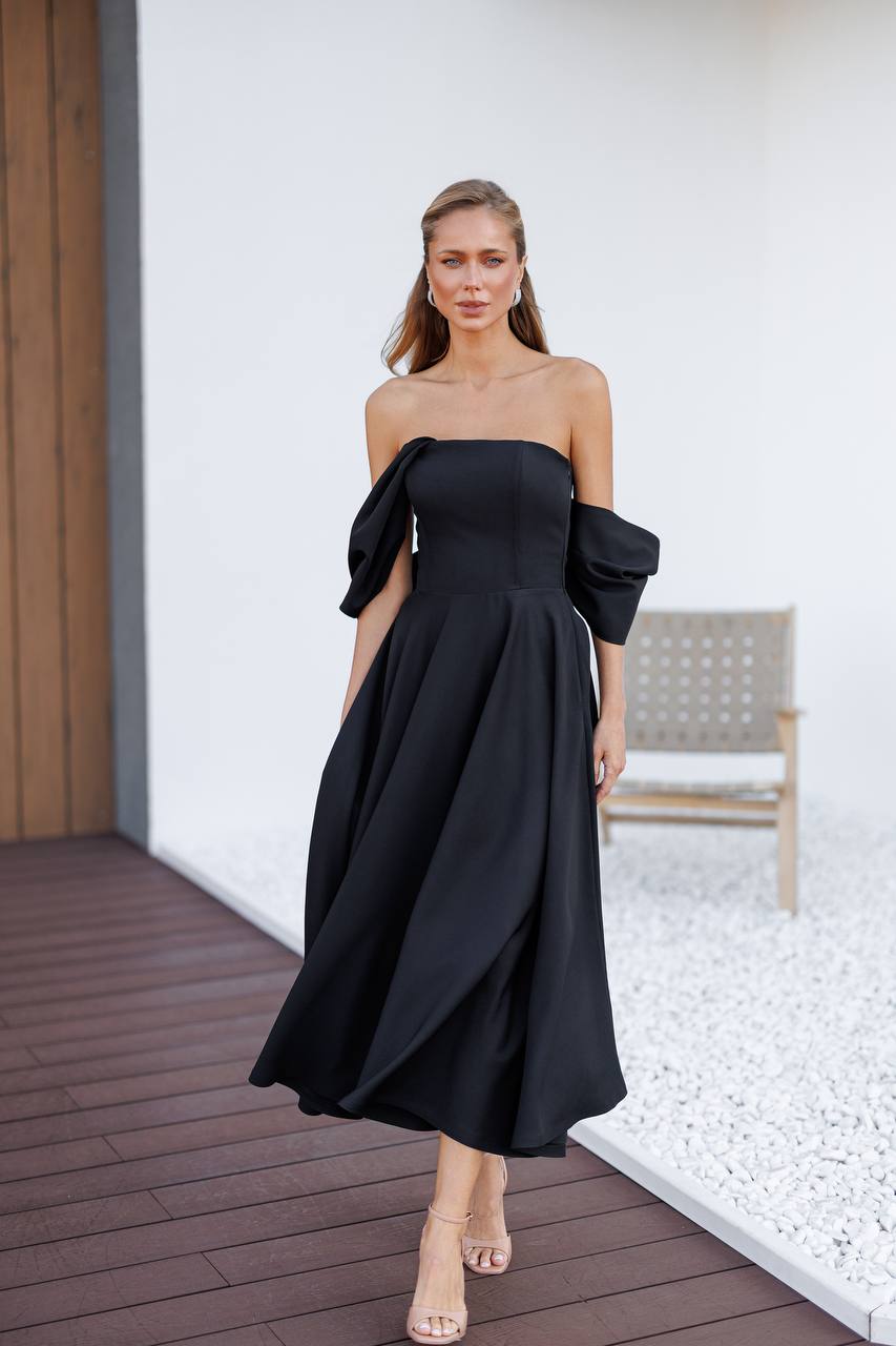 Woman wearing a black off-shoulder dress on a wooden deck.
