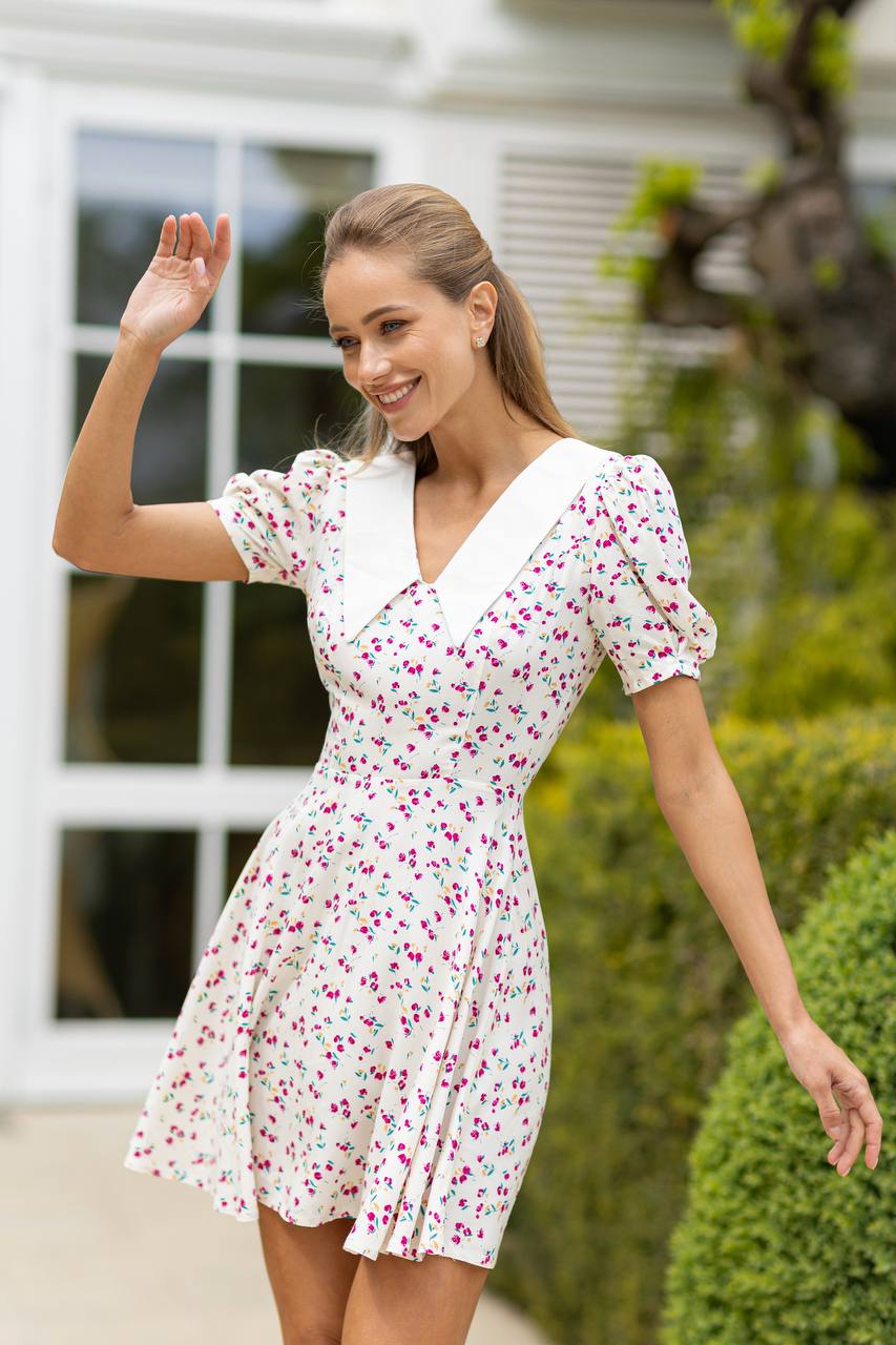 Woman in a white floral dress waving outdoors