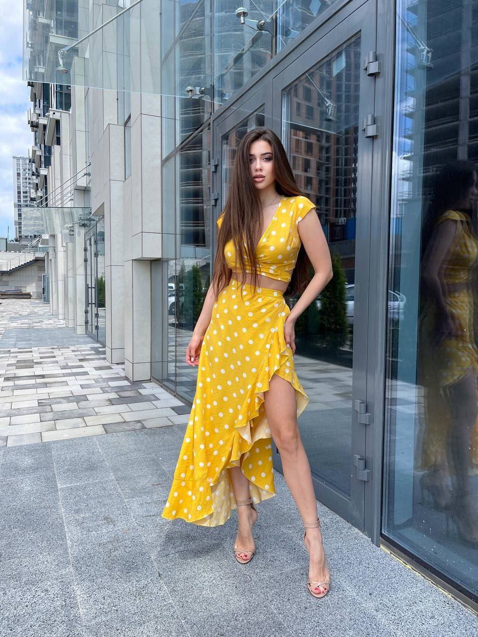 Woman in a yellow polka dot dress standing in front of a modern building.
