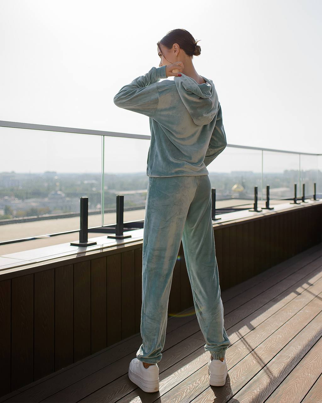 Person wearing a light blue tracksuit on a rooftop with a cityscape view.