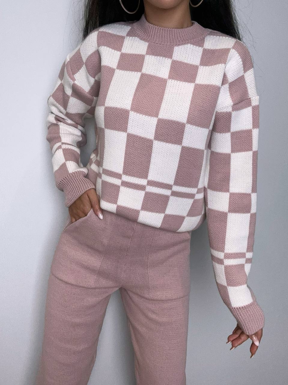 Person wearing a checkered sweater and pants set against a plain background