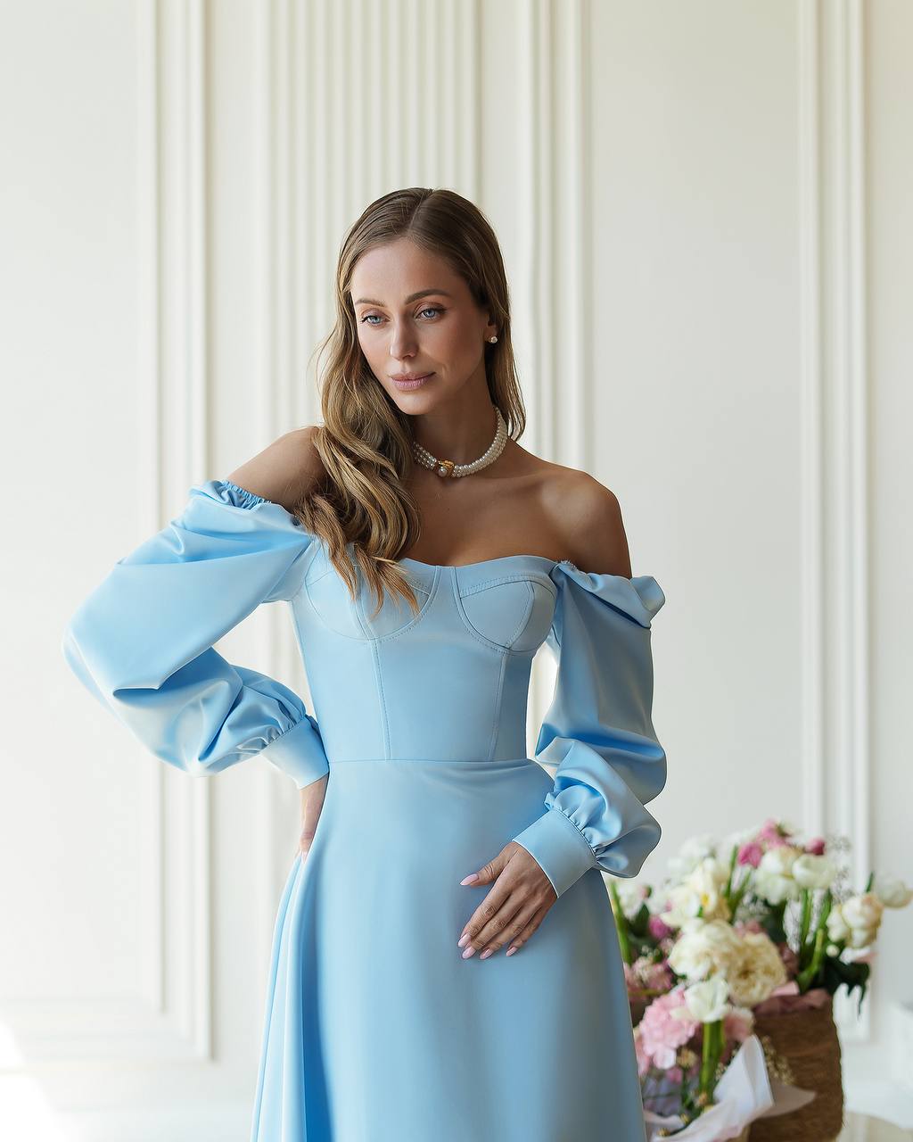 Woman wearing a light blue off-shoulder dress with puffed sleeves in an elegant indoor setting.
