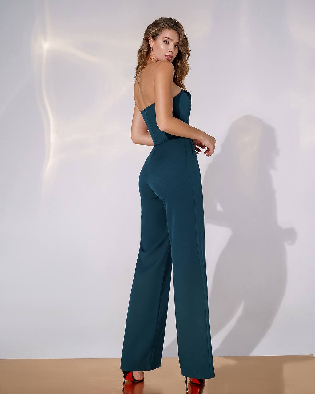 Woman wearing a strapless teal jumpsuit against a white background