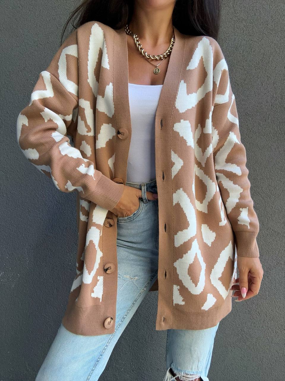 Person wearing a brown cardigan with white pattern, light blue jeans, and white sneakers against a gray background.