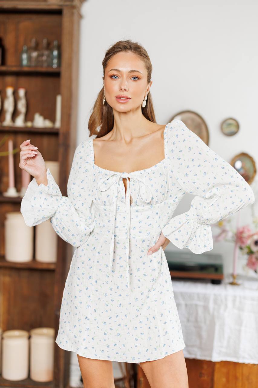 Woman wearing a white floral dress in a room with shelves and decor.