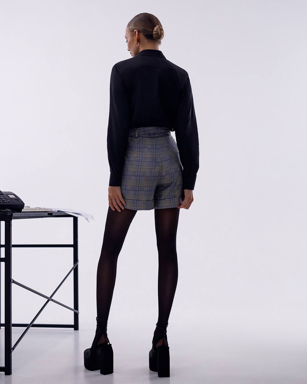 Person wearing a black top and plaid shorts on a white background