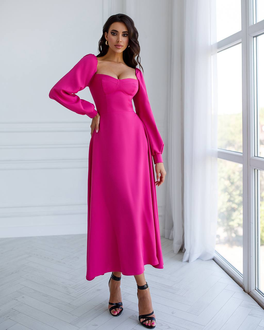 Woman wearing a bright pink dress in a bright room with large windows.