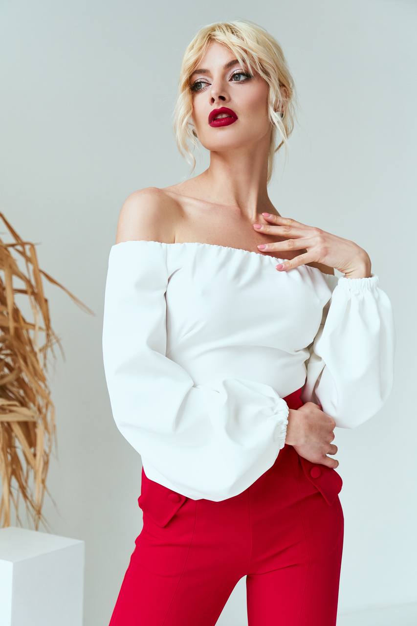 Woman wearing a white off-shoulder top and red pants against a light background