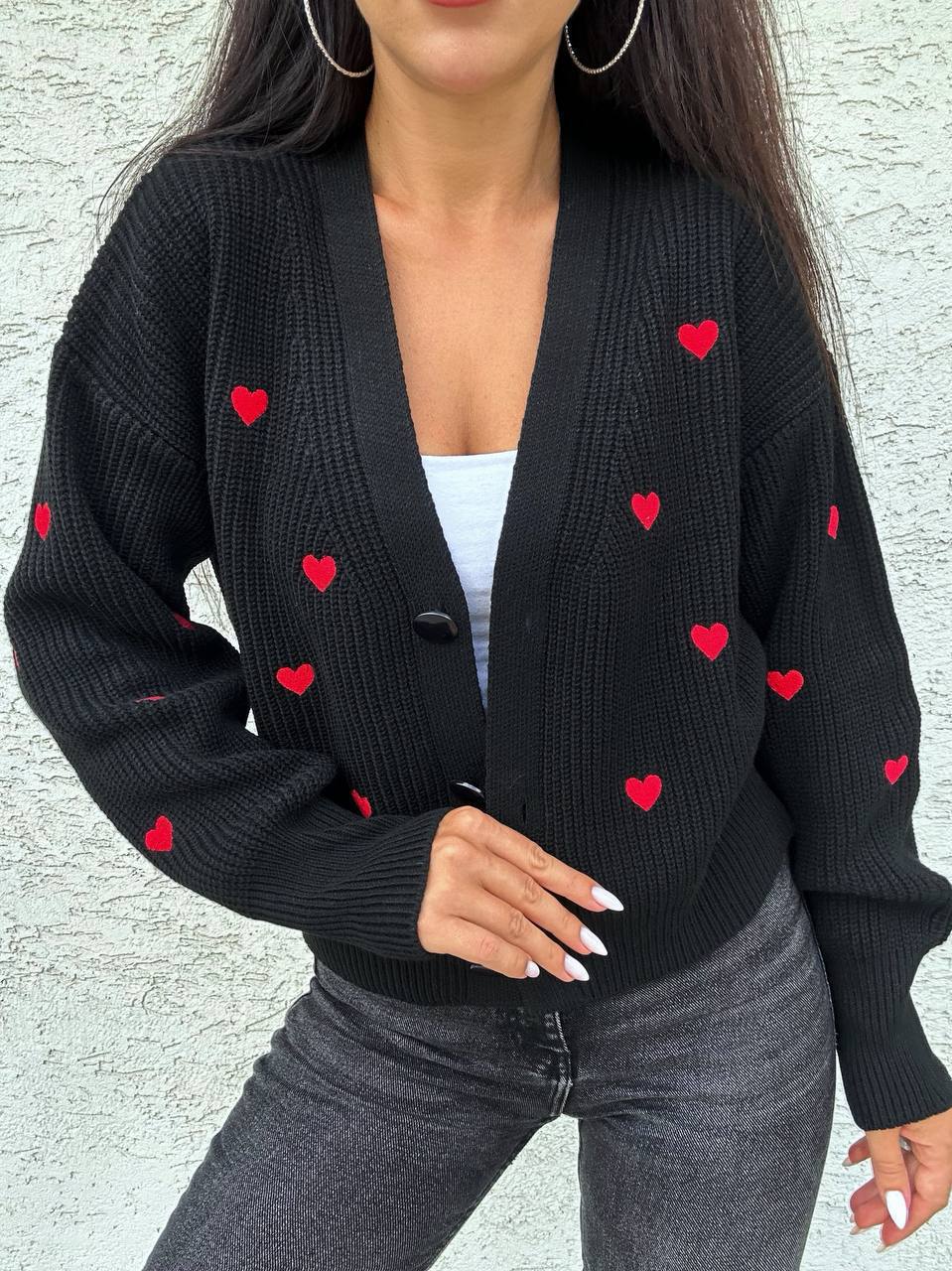 Black cardigan with red heart patterns worn by a person against a light gray background