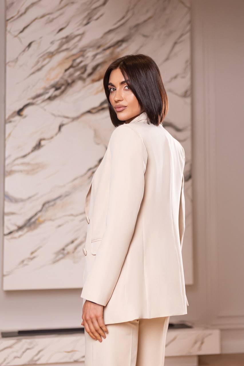 Woman wearing a beige suit standing in front of a marble wall.