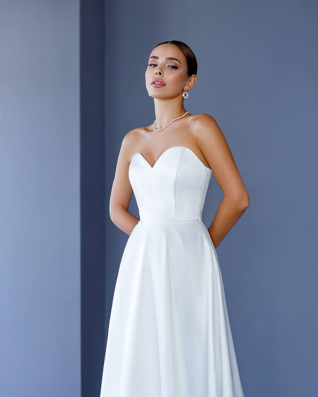 Woman wearing a strapless white wedding dress against a blue background