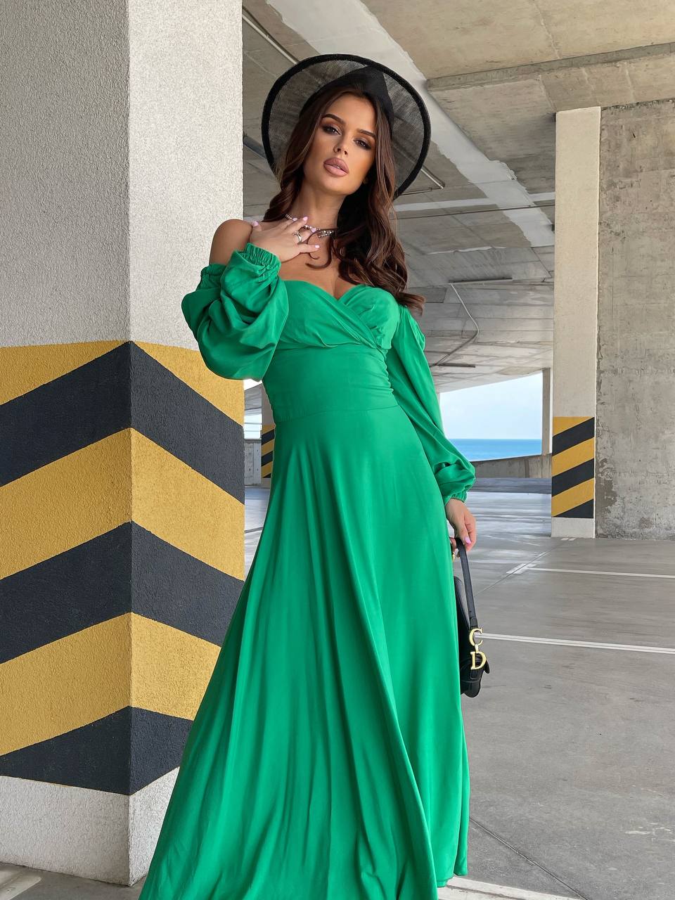 Woman in a green dress standing under a bridge with a geometric patterned wall.