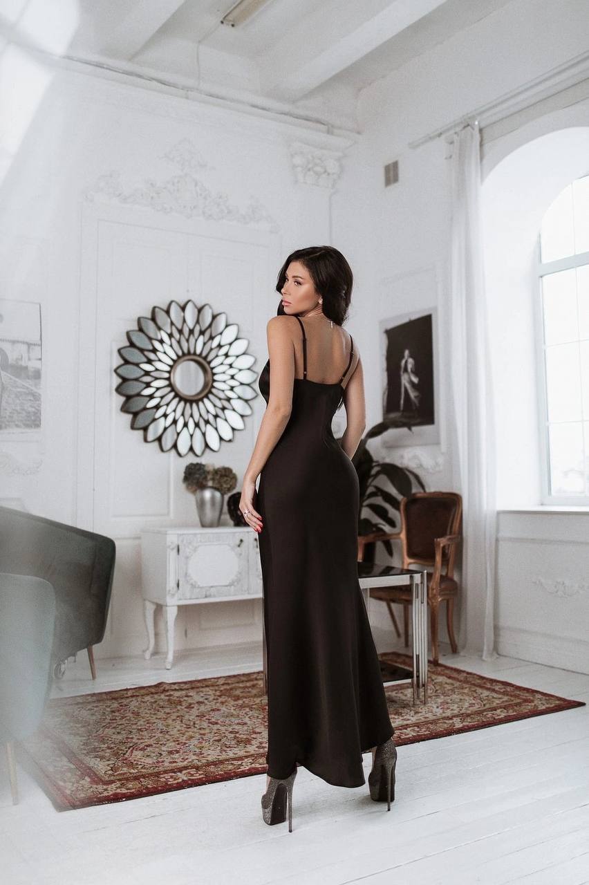 Woman in a black dress standing in a stylishly decorated room with white walls and a rug.