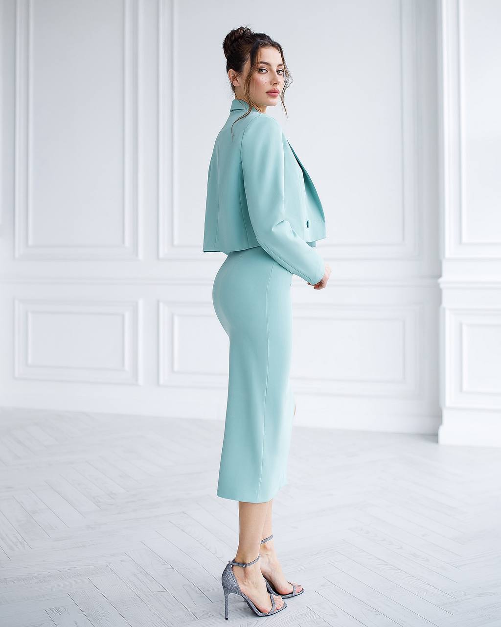 Woman wearing a light blue suit standing against a white wall.
