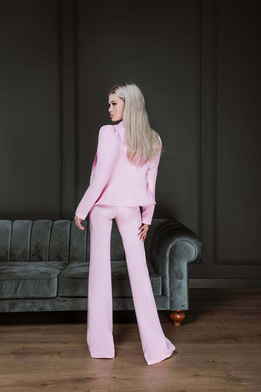 Woman in a pink suit standing in a room with a dark wall and green sofa.