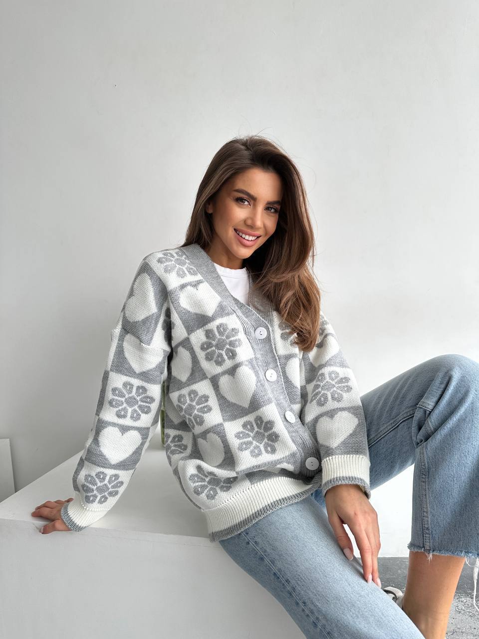 Woman wearing a patterned sweater sitting on a white surface with a light gray background