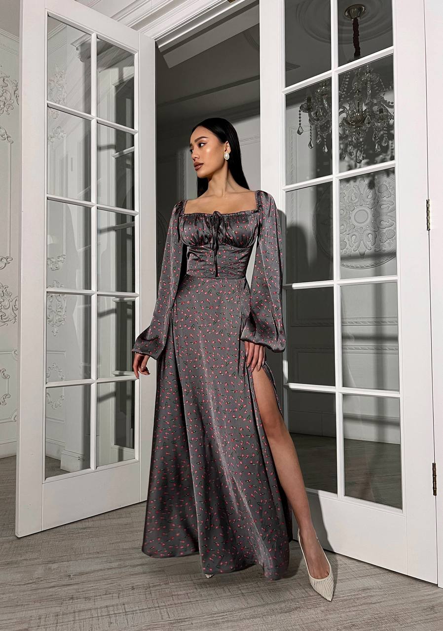 Woman in a long, dark patterned dress standing in a room with large windows.