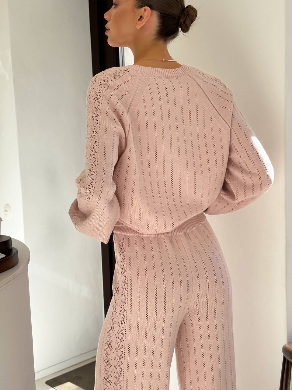 Person wearing a pink knit outfit with lace details in a minimal indoor setting.