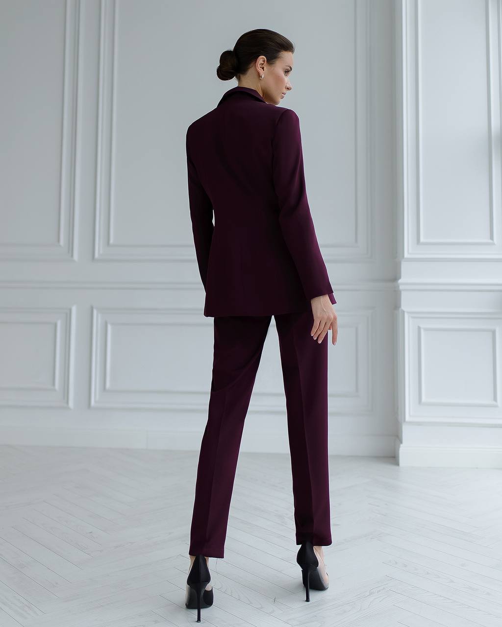 Woman wearing a burgundy suit standing in a room with white paneled walls.