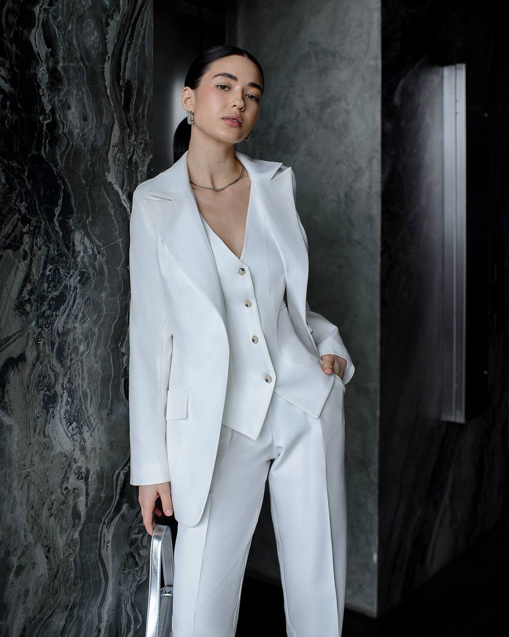 Woman wearing a white suit against a dark marble wall
