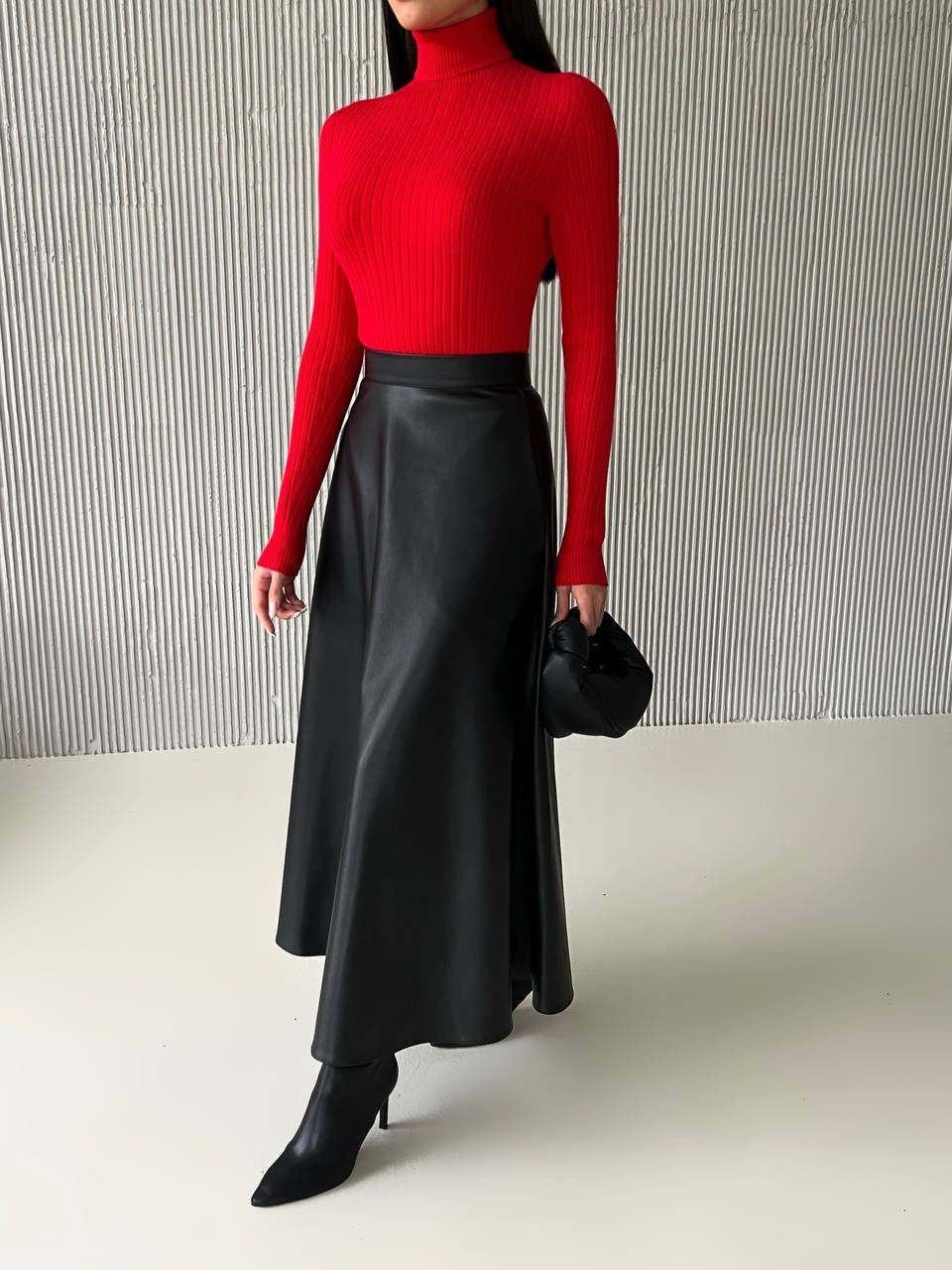 Person wearing a red turtleneck and black leather skirt against a neutral background