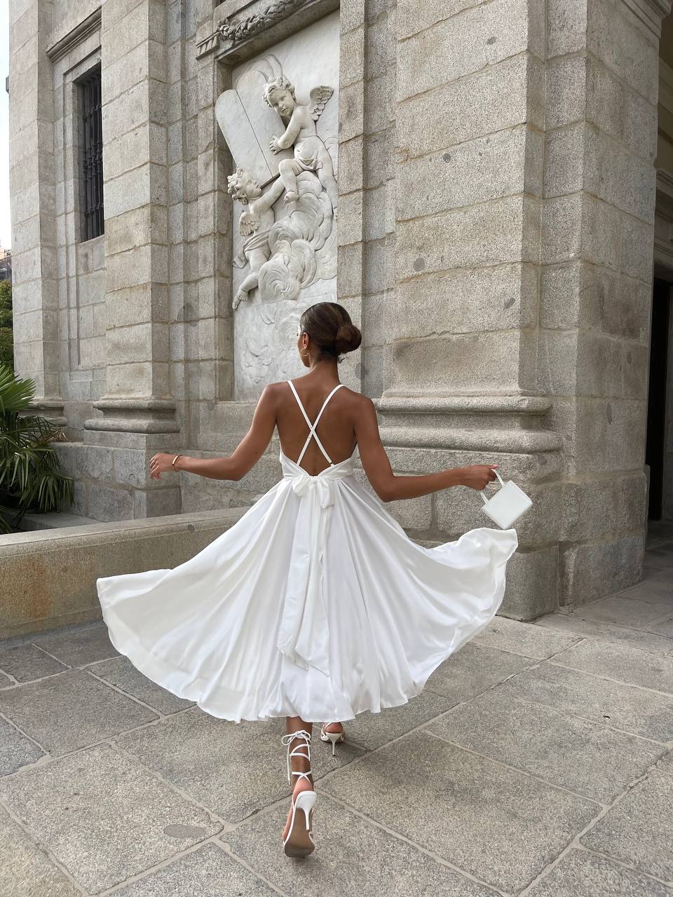 Woman in a white dress standing in front of a stone building with architectural details.