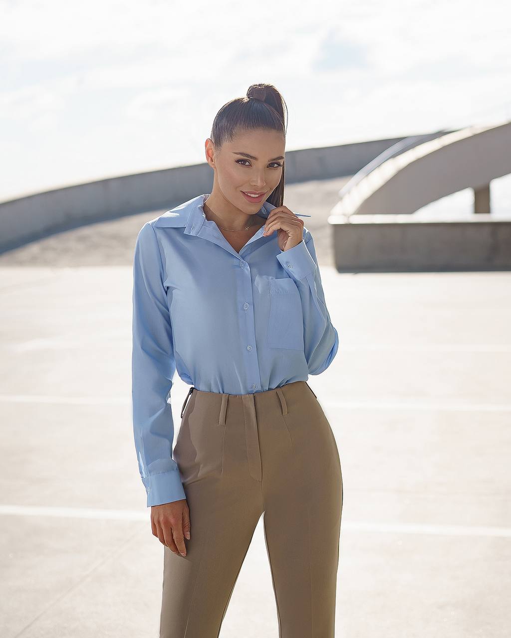 Woman wearing a light blue shirt and beige pants standing outdoors.