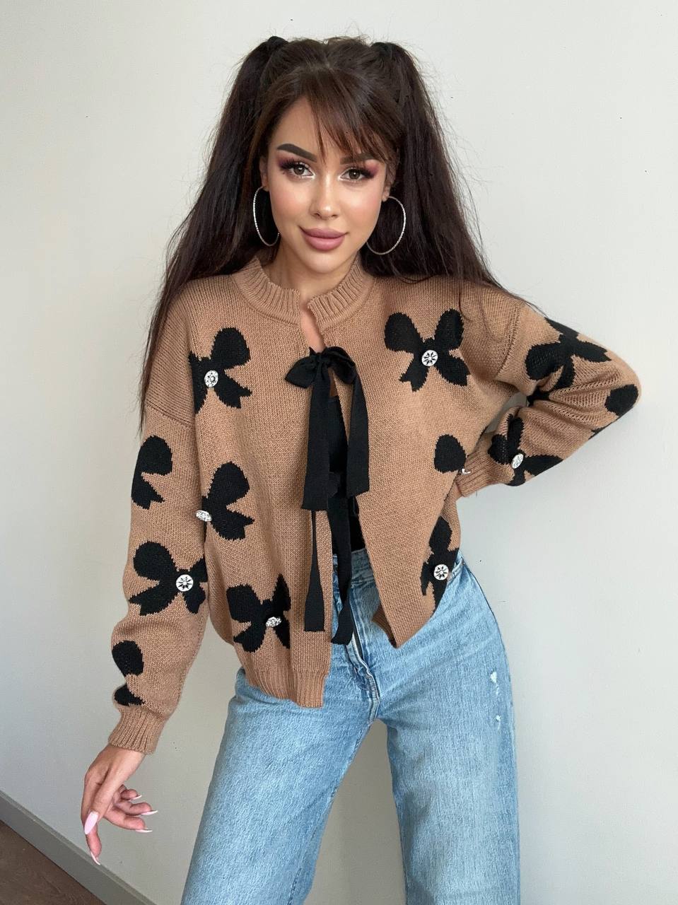Woman wearing a brown sweater with black floral patterns and blue jeans against a plain background