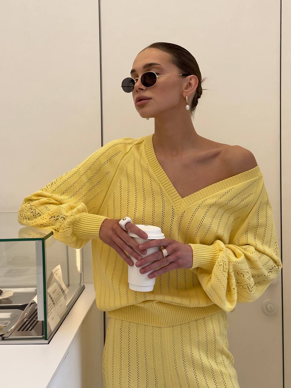 Woman wearing a yellow outfit holding a coffee cup indoors.